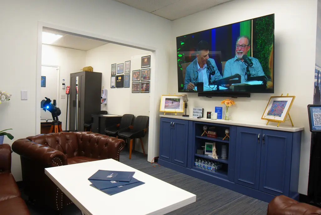 The 75-inch TV in the green room showing a podcast being recorded